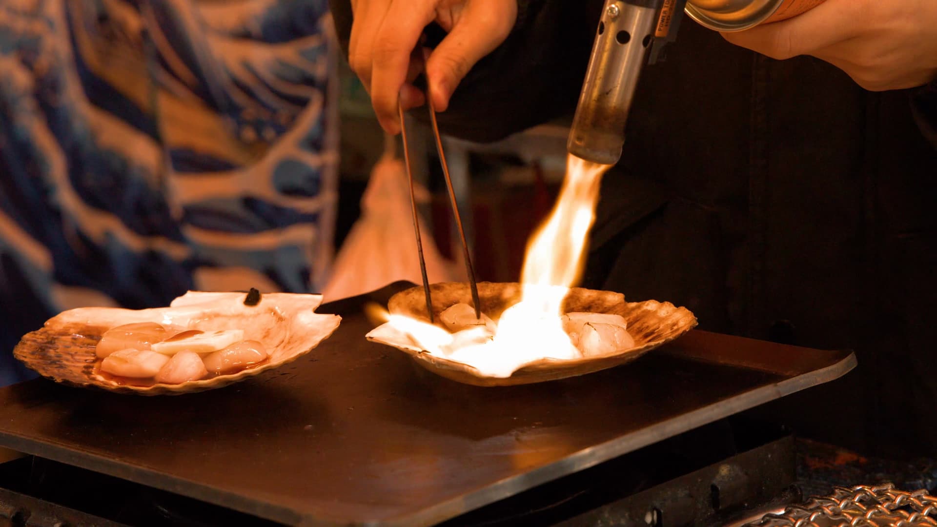 Scallops being flame-seared in their shells at a street food stall